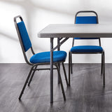 Blue banqueting chairs around a grey folding table.