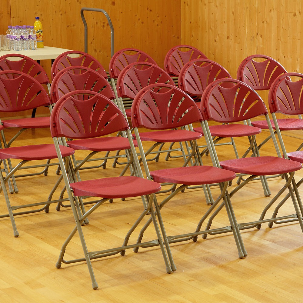 Burgundy fan back plastic folding chairs in rows in hall.