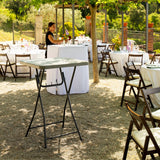 Outdoor event setup with tables, chairs, and a person in a garden setting.