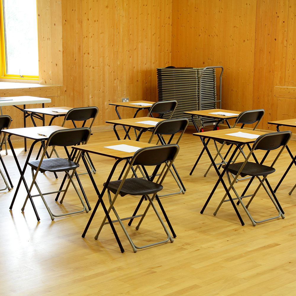 Folding chairs and folding exam desks set up in school hall for exams.