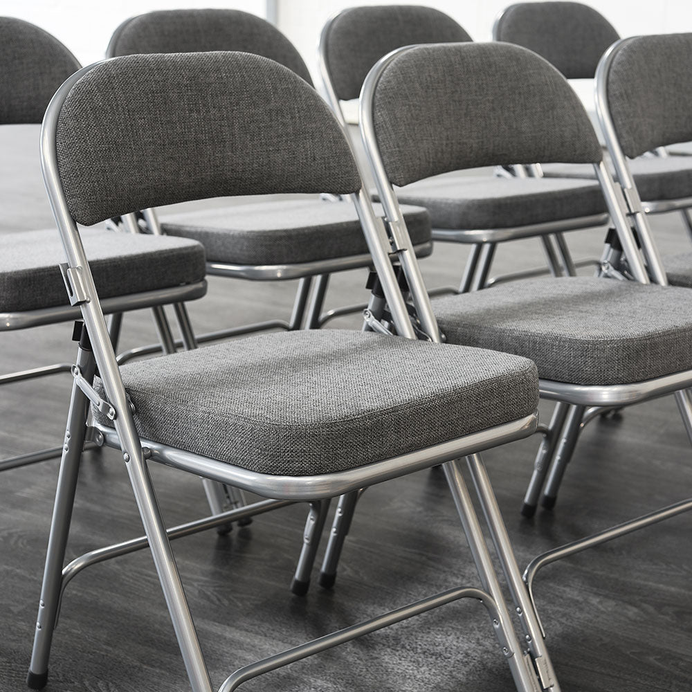 Rows of padded folding chairs with grey upholstery and silver frames.